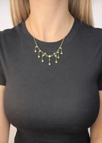 A yellow gold swag necklace with peridot drops, modelled by a woman wearing a black top