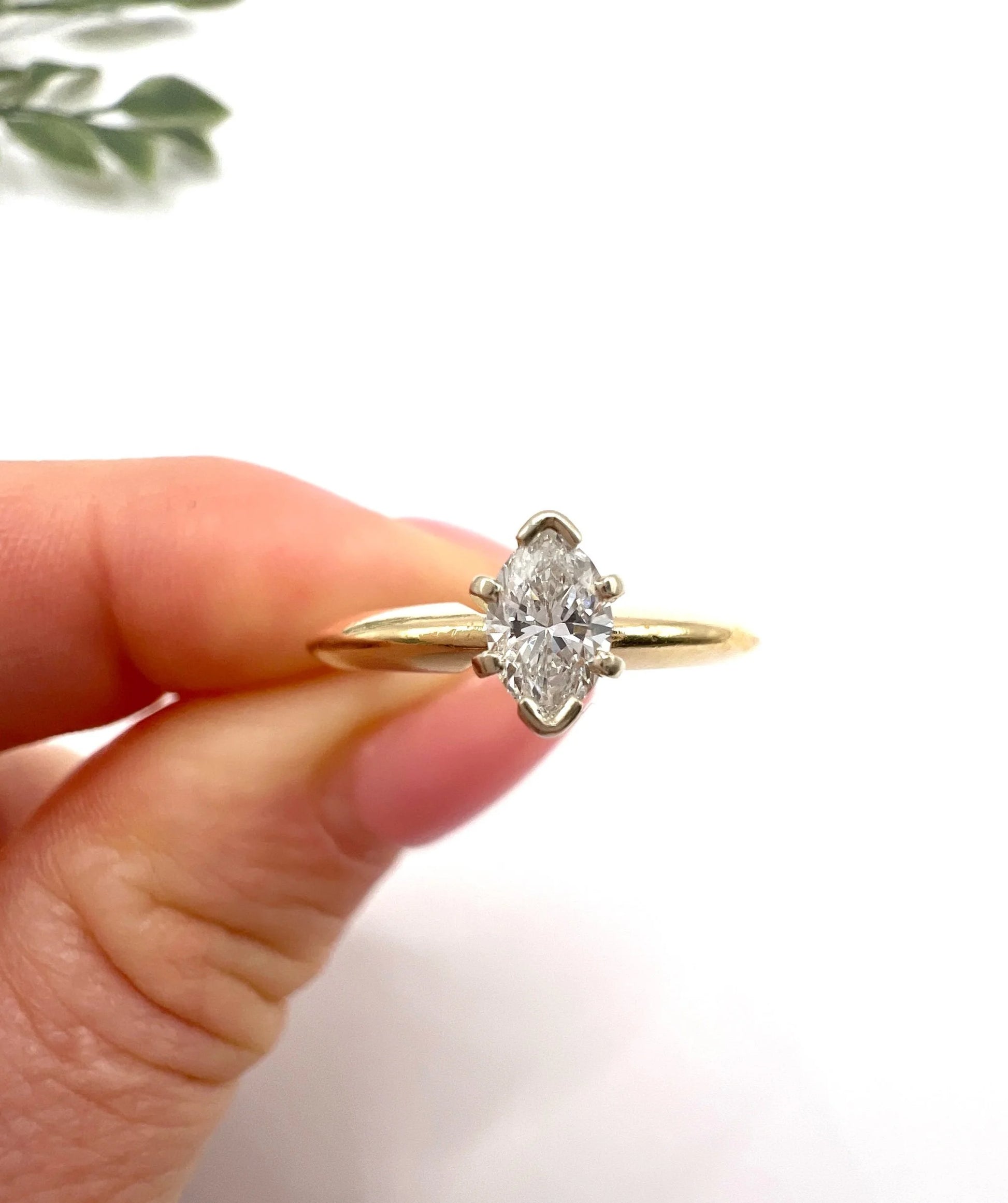A marquise diamond solitaire ring in yellow and white gold, held in a hand