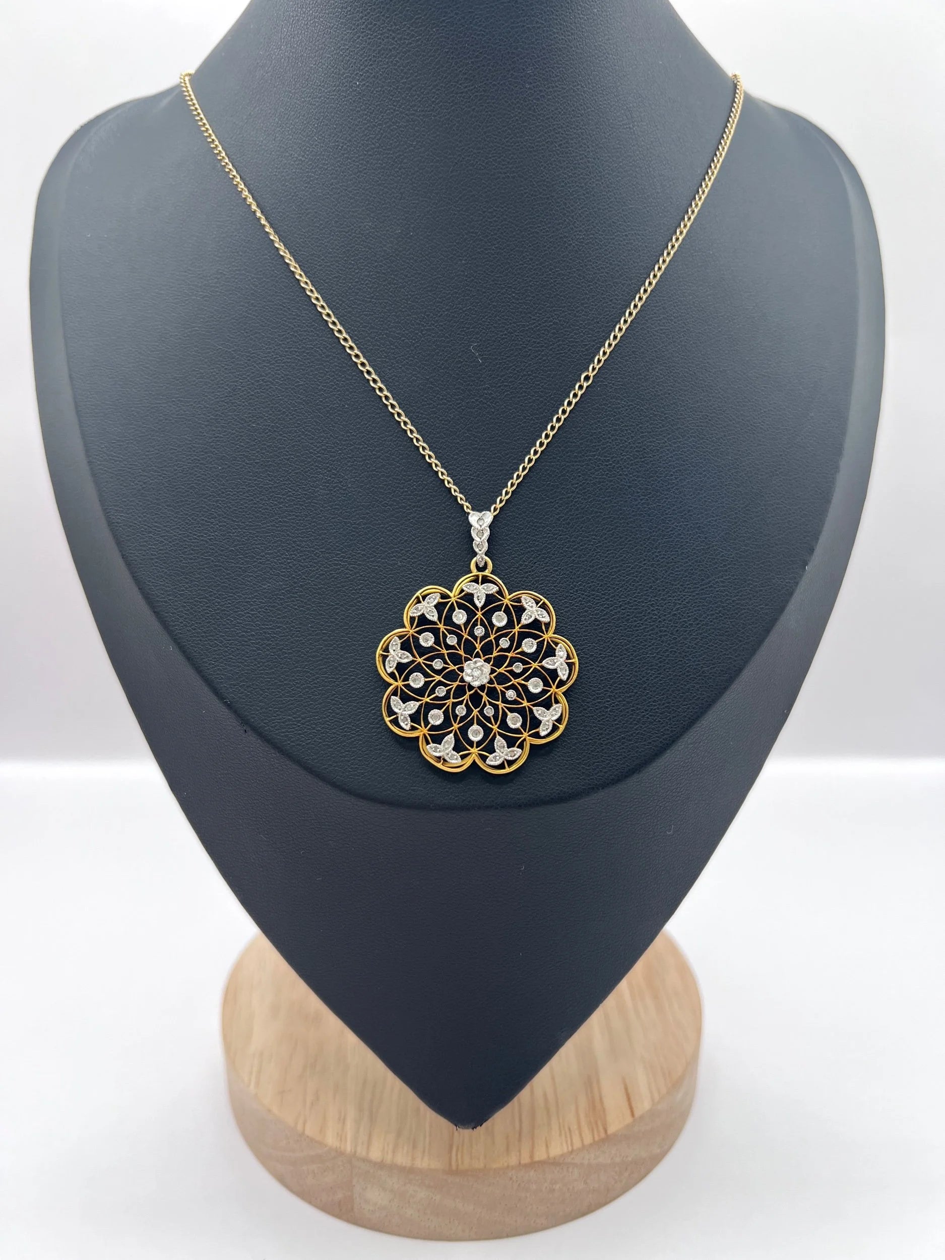 A floral openwork diamond pendant in gold and platinum, with a chain, on a black jewellery bust