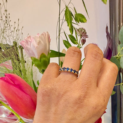 A seven stone round sapphire band ring in yellow gold, modelled on a hand