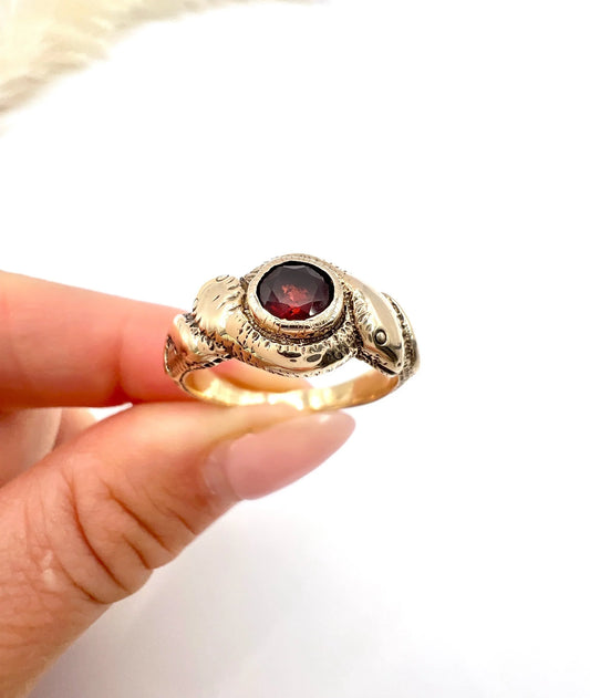 A double headed snake ring in gold with a garnet centre, held in a hand