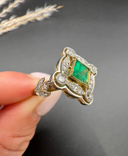 A gold and platinum ring with a centre emerald and diamond surround, held in a hand