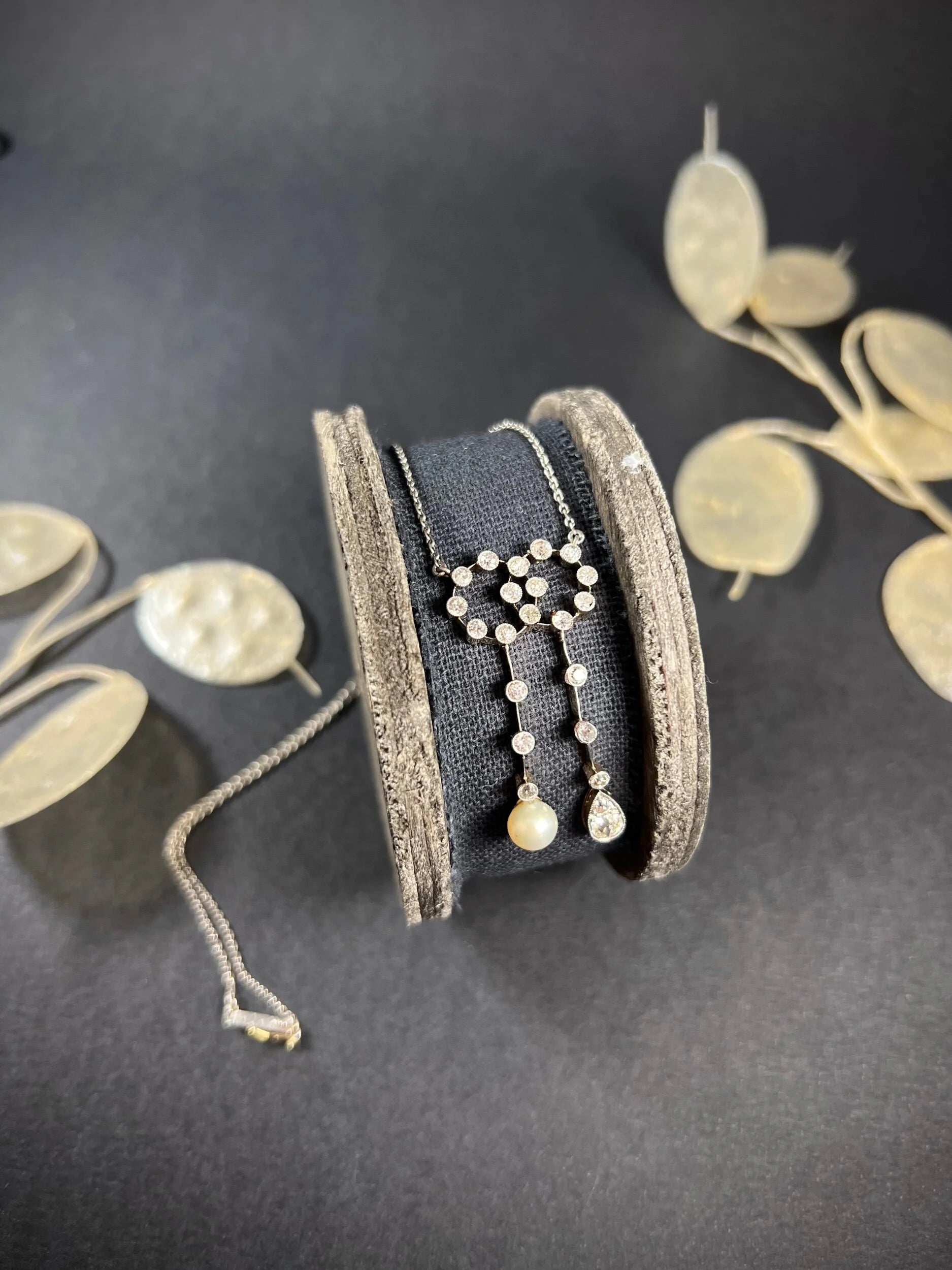An antique diamond and pearl double drop pendant necklace, on a wooden spool