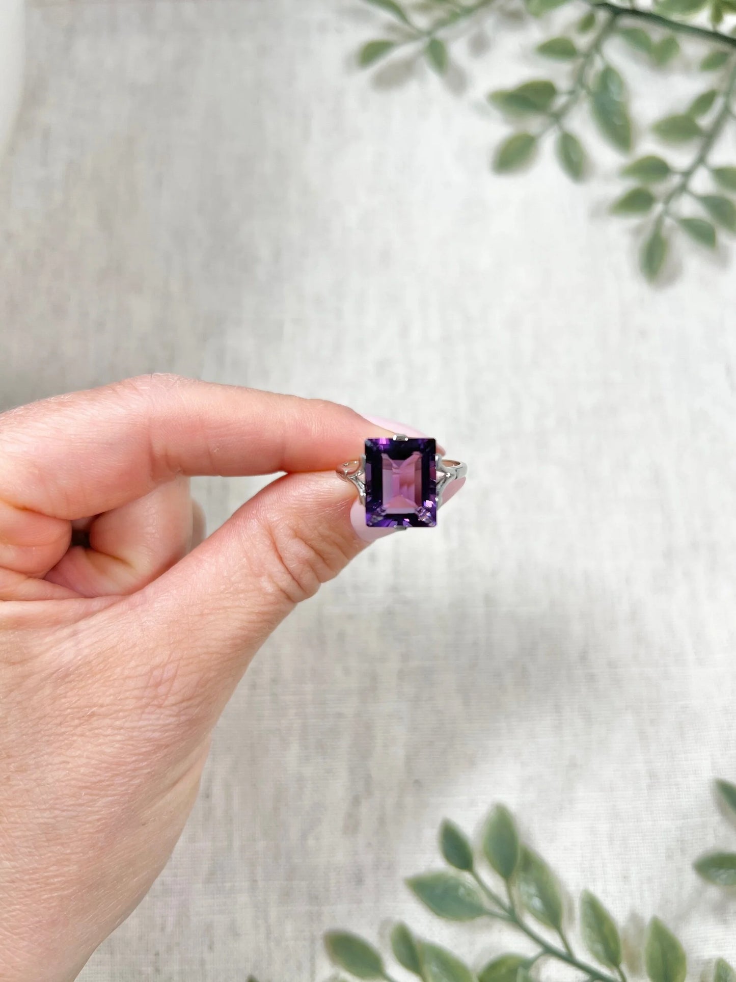 A solitaire amethyst cocktail ring in platinum, held in a hand