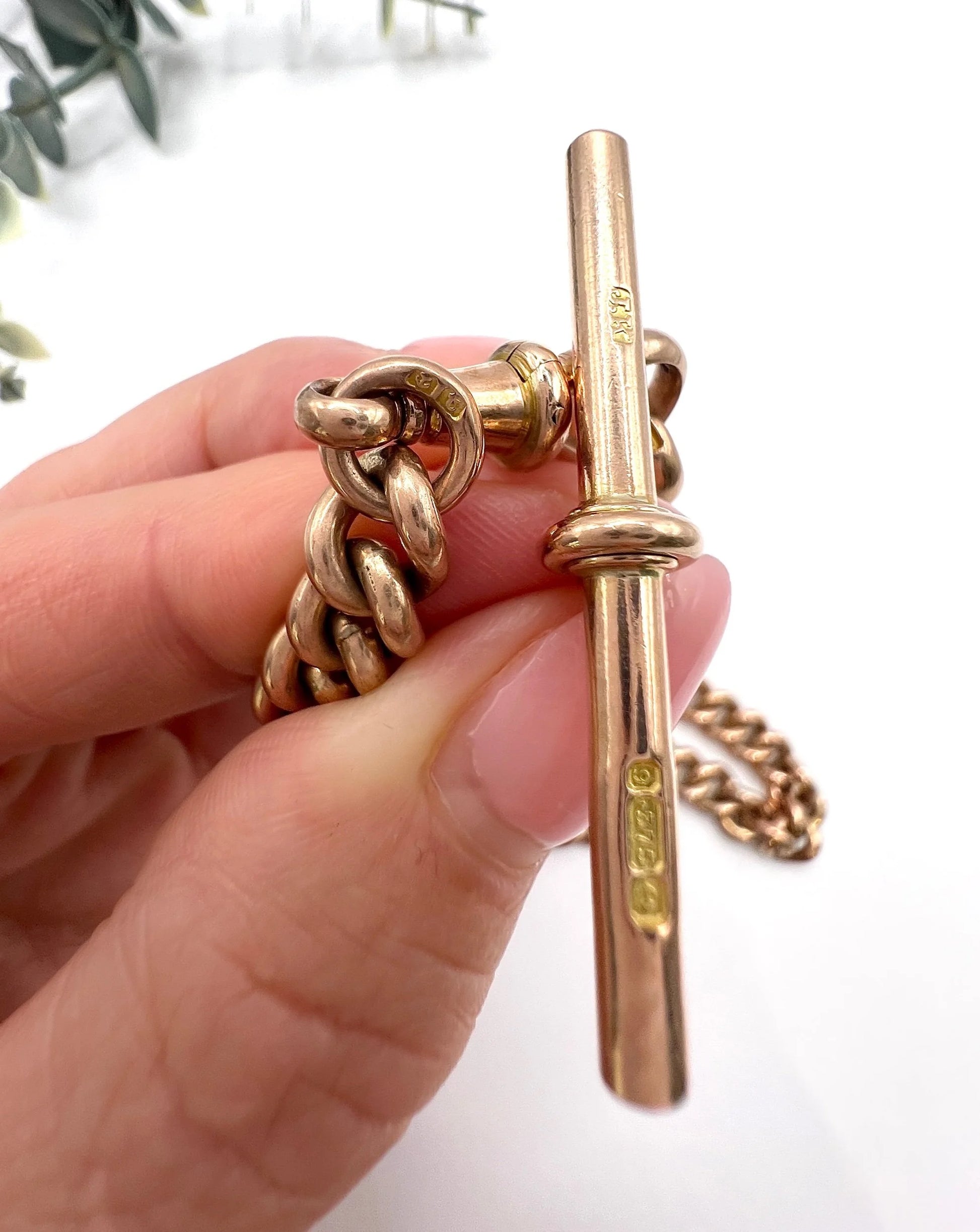 Close-up of a rose gold T-bar and curb links held in a hand