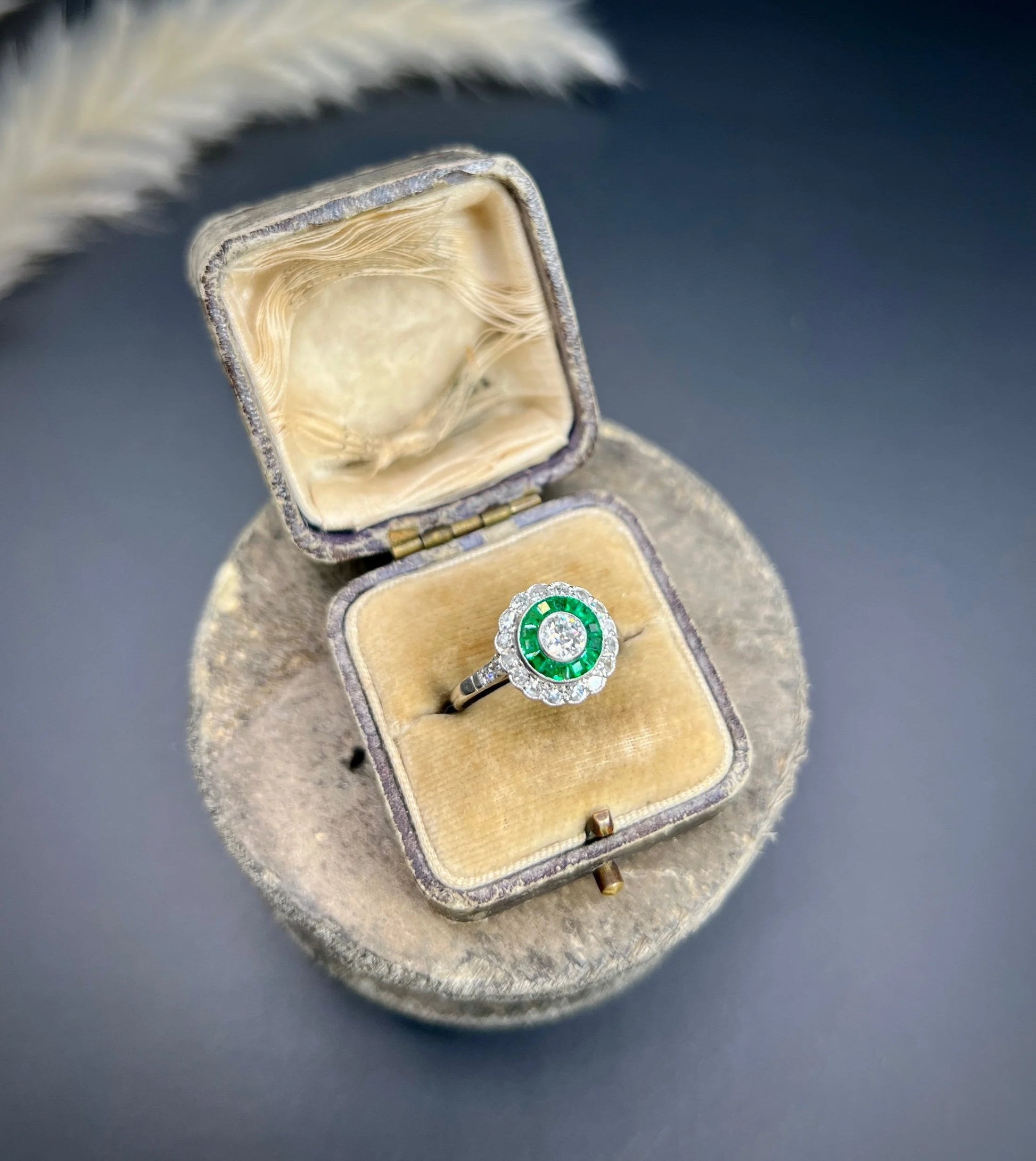 An emerald and diamond target cluster ring in platinum, in a ring box