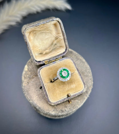 An emerald and diamond target cluster ring in platinum, in a ring box
