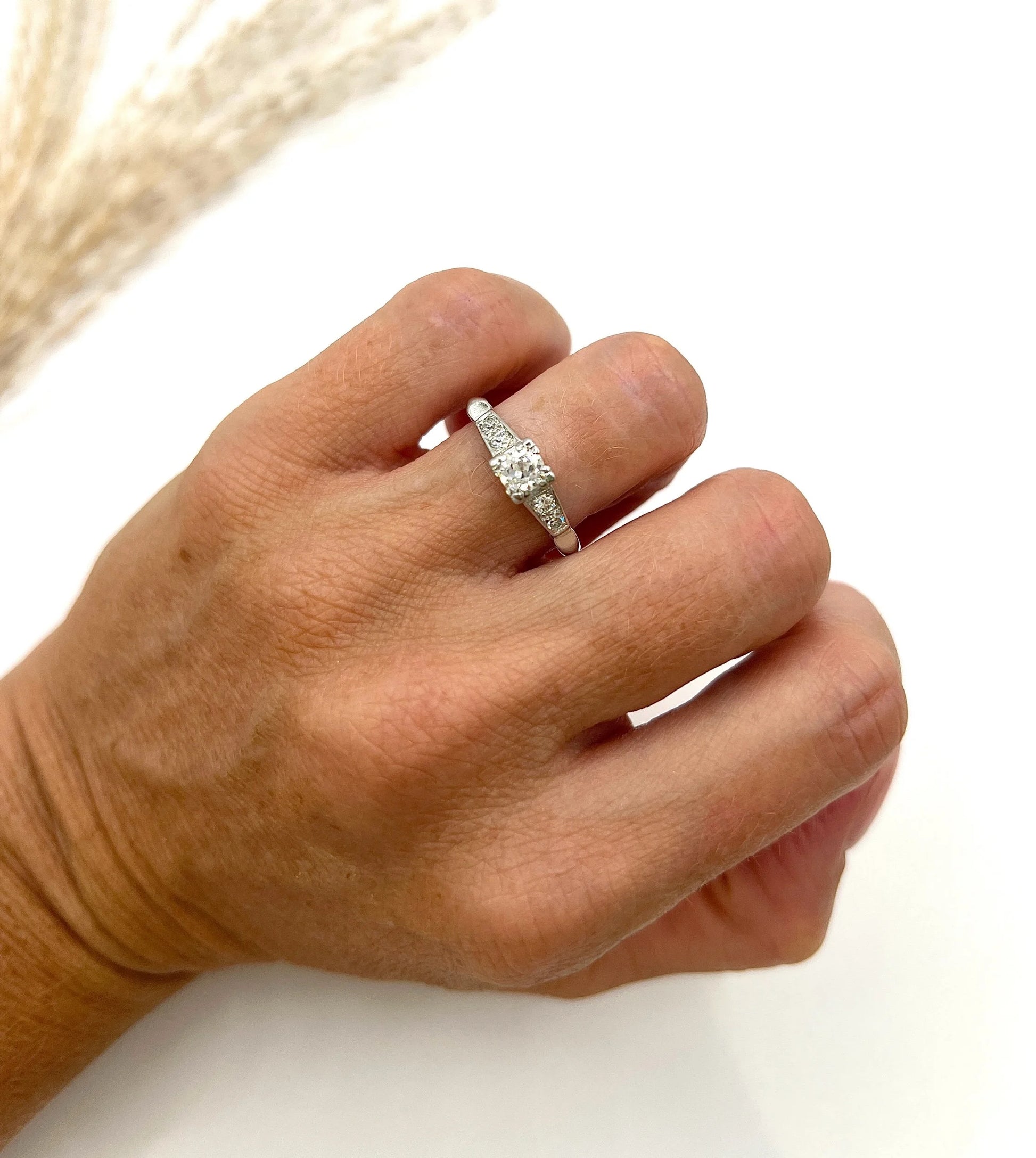 A solitaire diamond ring in platinum, with diamond set shoulders, modelled on a hand