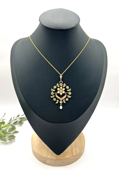 A peridot and pearl floral circle brooch/pendant in yellow gold, with a chain, on a black jewellery bust