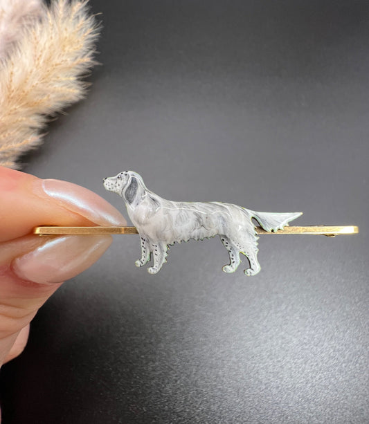 An enamelled dog bar brooch in yellow gold, held in a hand