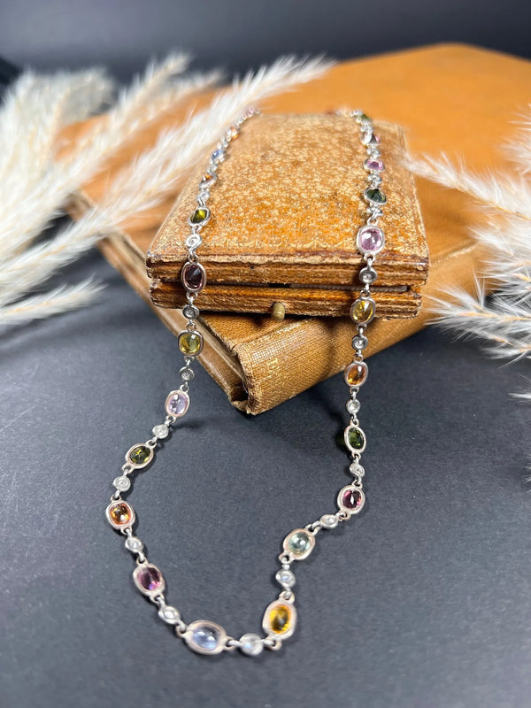 A coloured sapphire and diamond set necklace in platinum and gold, on an antique box and antique book