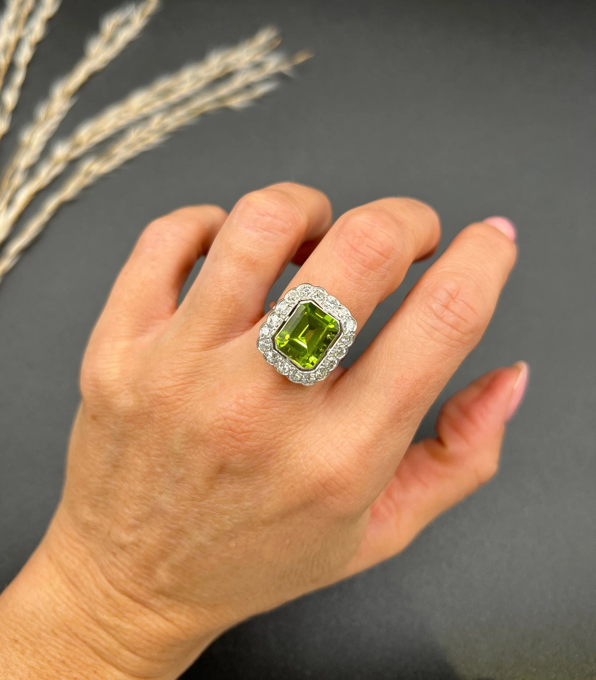 A cushion shaped peridot and diamond cluster ring in white metal, modelled on a hand