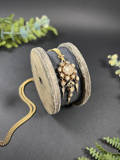A yellow gold pendant with old cut diamonds, with a gold chain, on a wooden spool