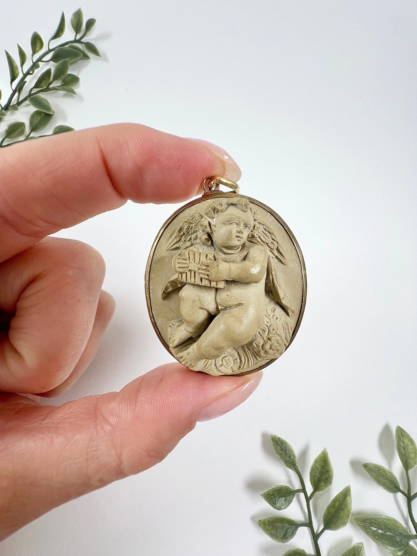 An oval cherub lava cameo pendant in yellow gold, held in a hand