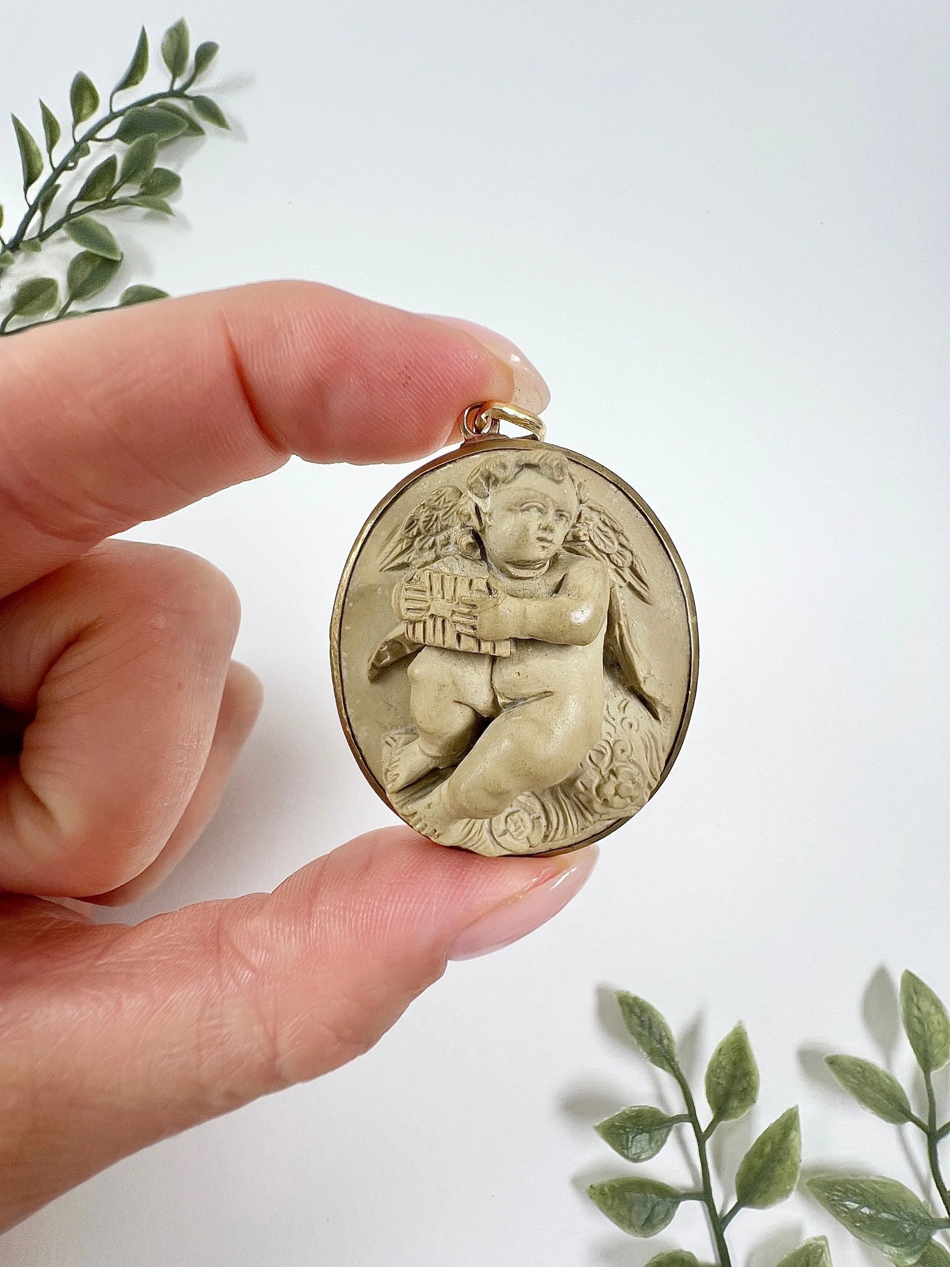 An oval cherub lava cameo pendant in yellow gold, held in a hand