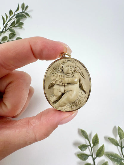 An oval cherub lava cameo pendant in yellow gold, held in a hand