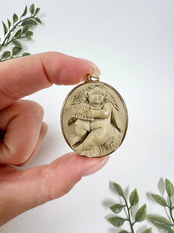 An oval cherub lava cameo pendant in yellow gold, held in a hand