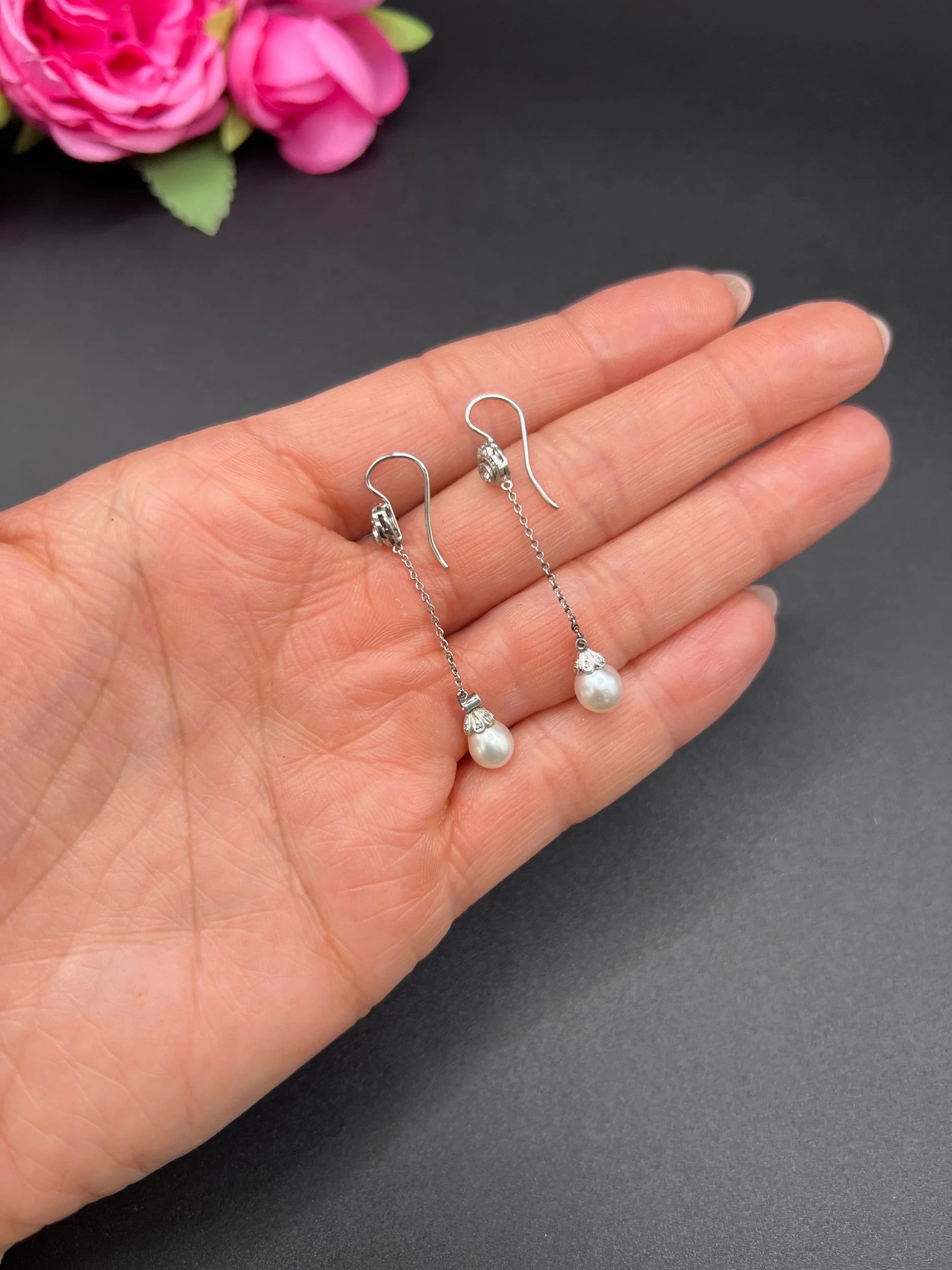 A pair of long drop platinum earrings with pearls and diamonds, held in a hand