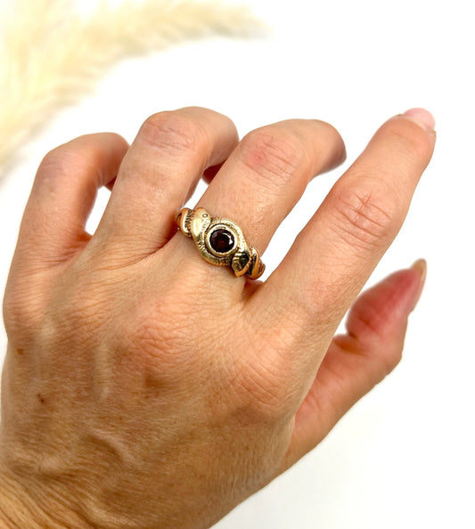 A double headed snake ring in gold with a garnet centre, modelled on a hand