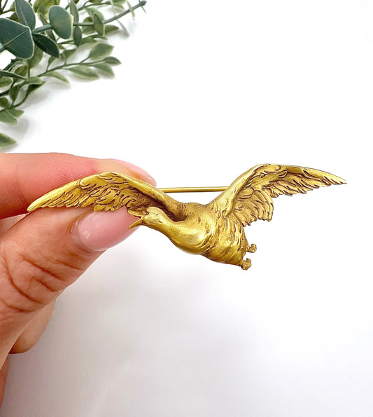 A yellow gold flying goose brooch, held in a hand