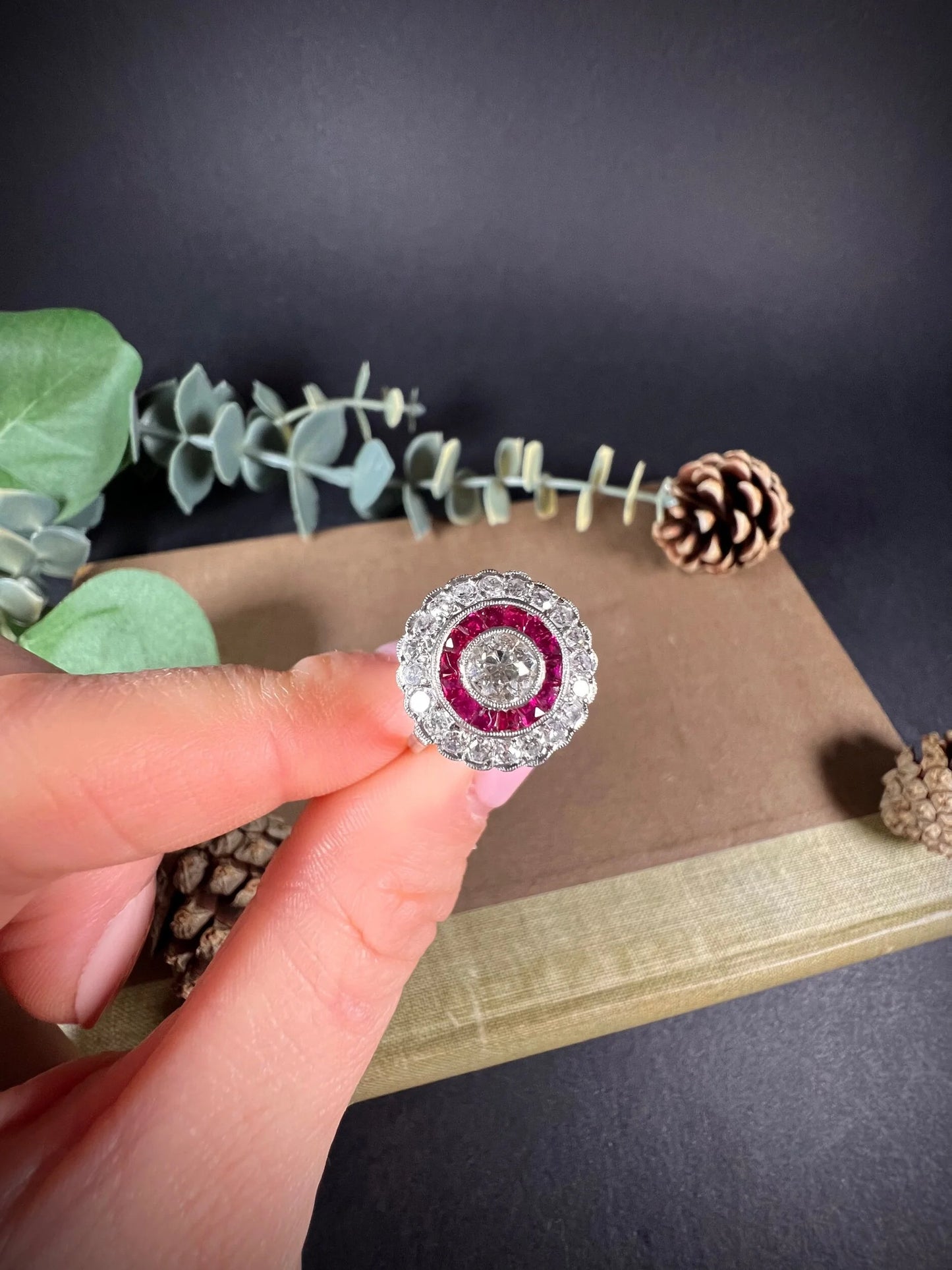 A round cluster ring with rubies and diamonds in white gold, held by a hand