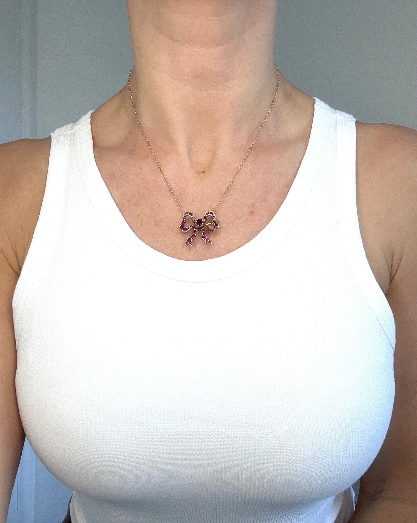 A ruby bow brooch necklace in gold and silver, modelled by a woman wearing a white top