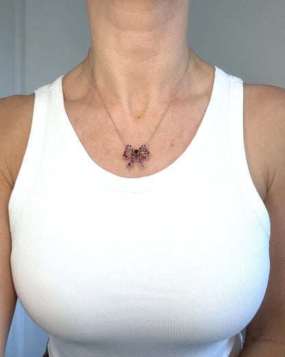 A ruby bow brooch necklace in gold and silver, modelled by a woman wearing a white top