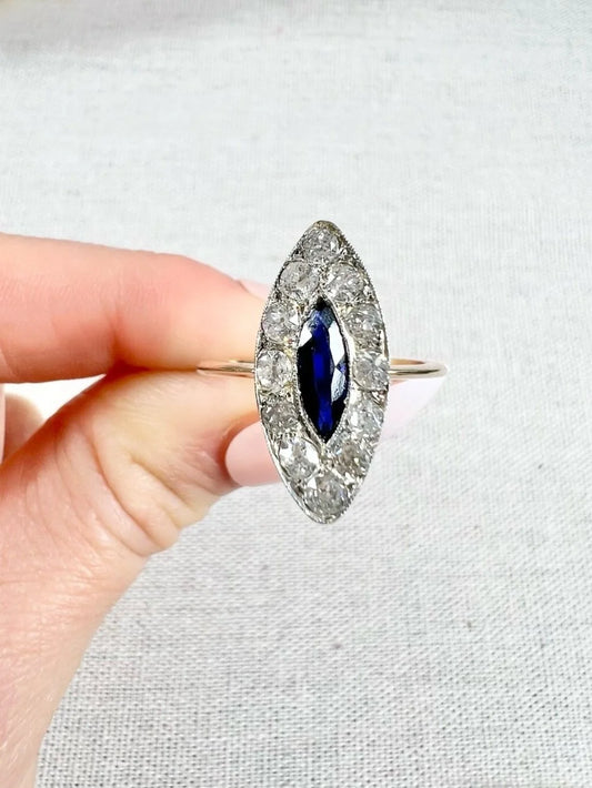 A navette shaped sapphire and diamond cluster ring in yellow gold and platinum, held in a hand