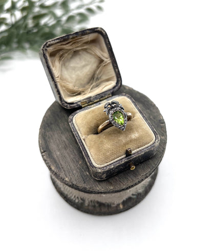 A pear cut peridot and round diamond cluster ring with bow detail, in yellow gold and white metal, in a ring box