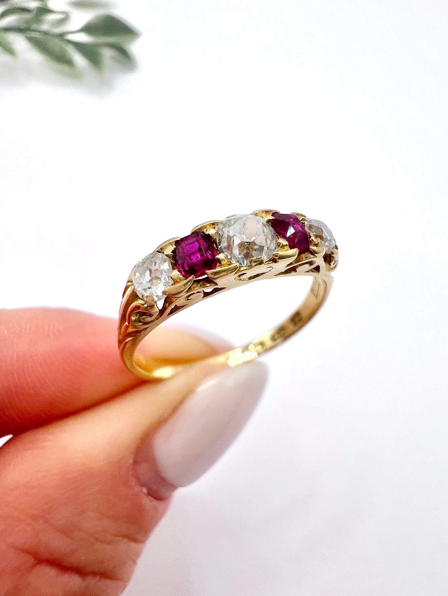 A yellow gold ruby and diamond five stone ring, held in a hand