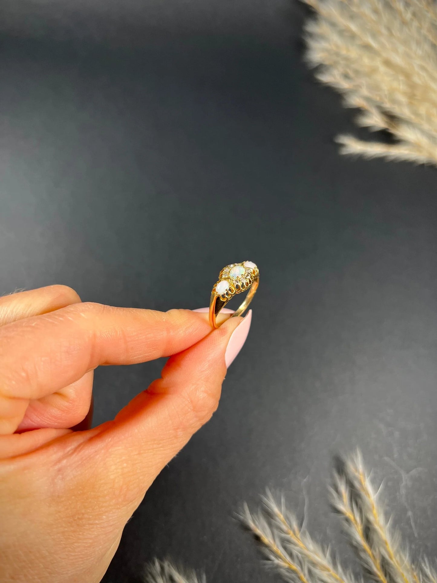 A yellow gold opal and diamond dress ring, held in a hand