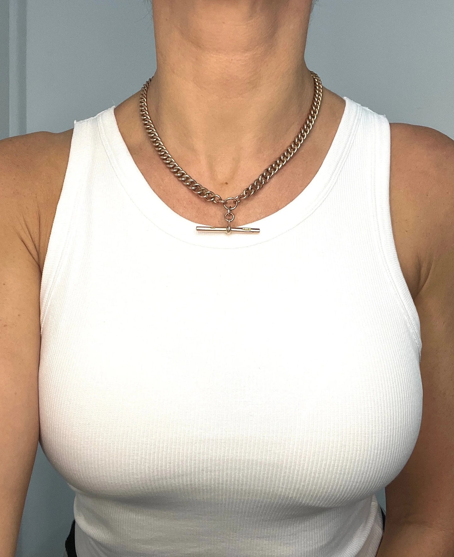 A rose gold curb link Albert chain modelled by a lady wearing a white top