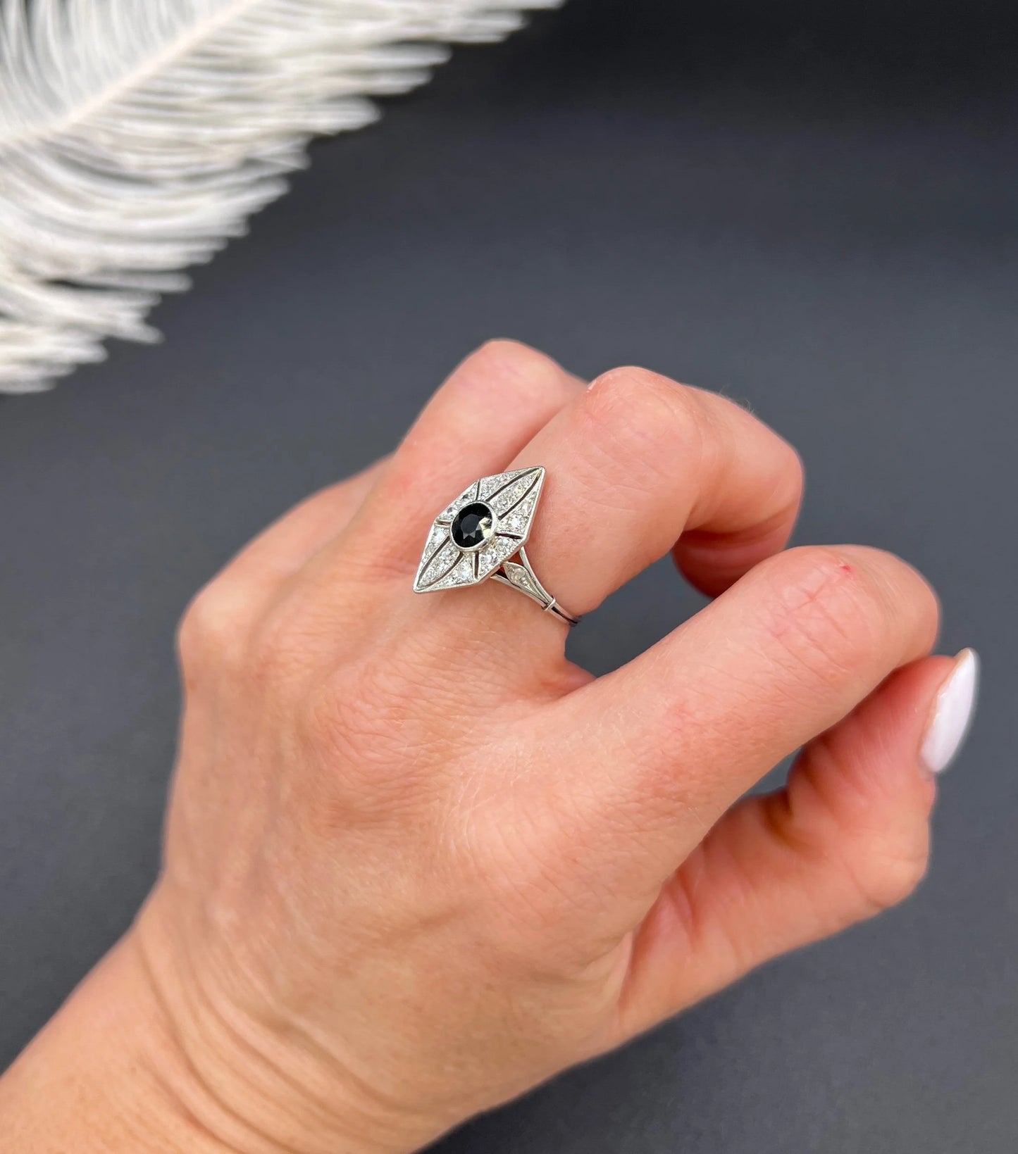 A navette shaped cluster cocktail ring with a sapphire centre surrounded by diamonds, in platinum, modelled on a hand