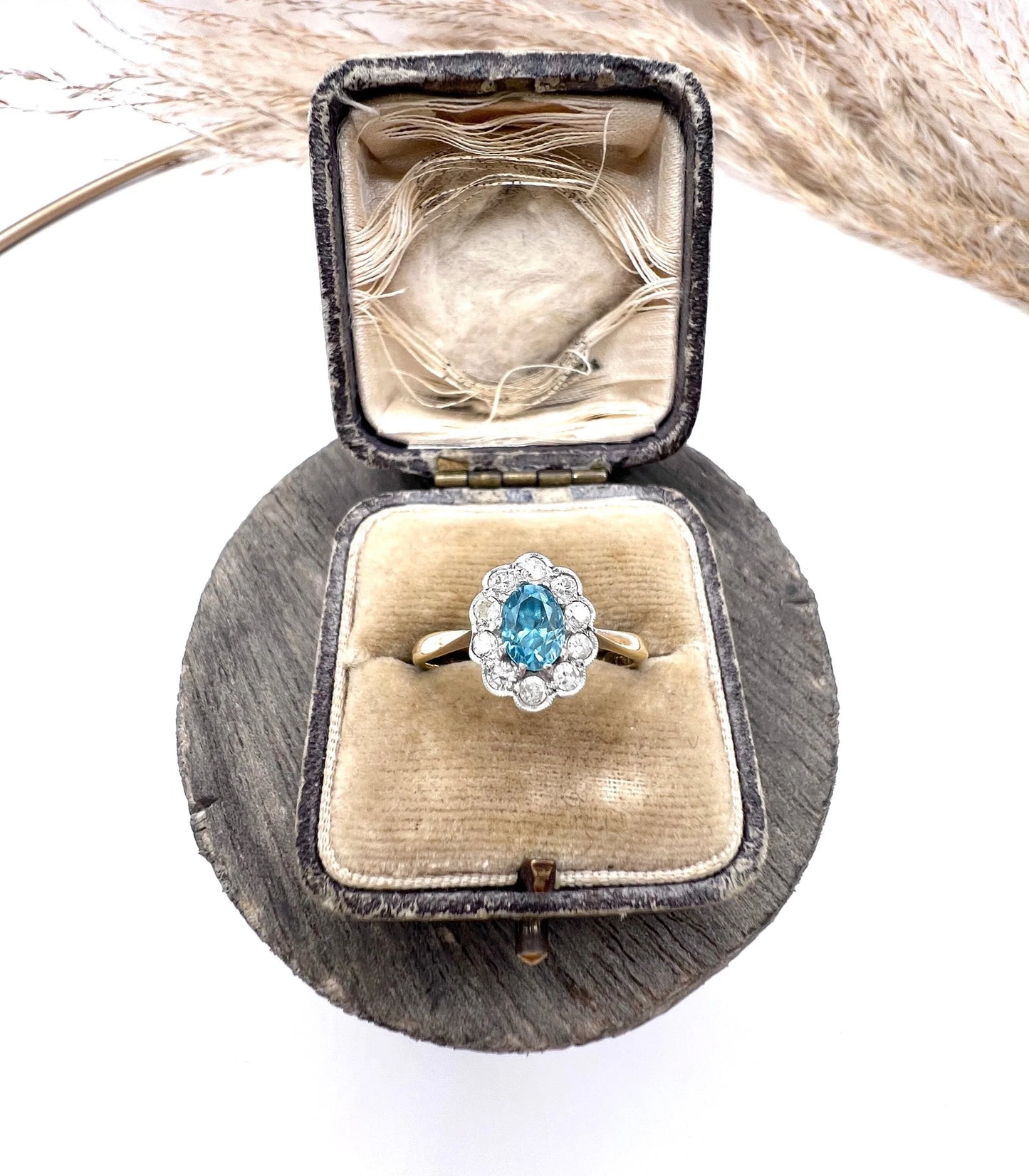 An oval cluster ring with a blue zircon centre surrounded by round diamonds, in yellow gold and platinum, in an antique ring box
