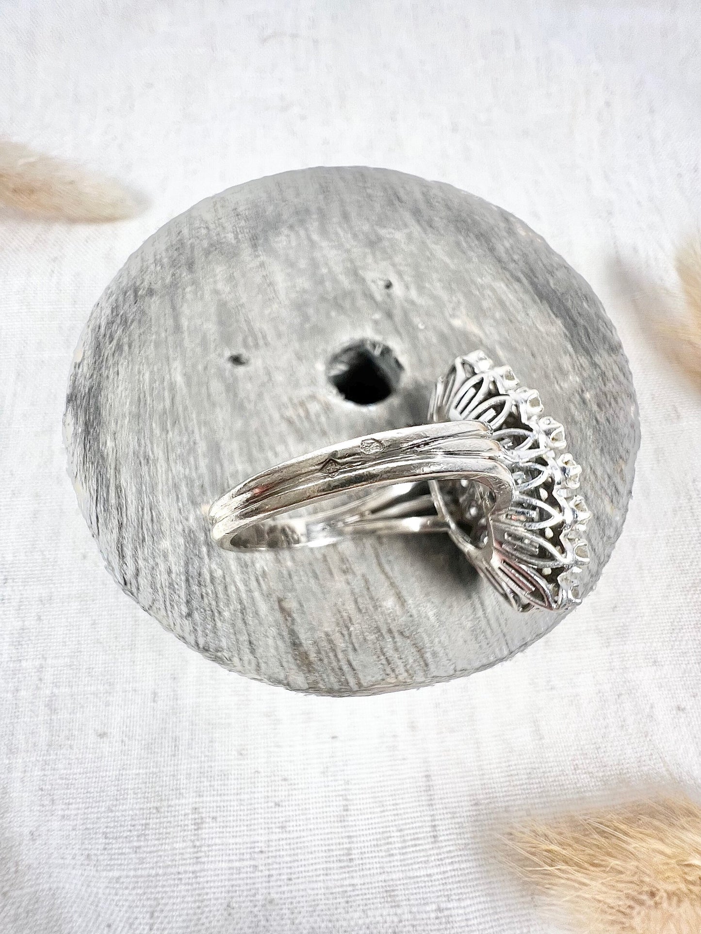 A navette shaped diamond cluster ring in white metal, sitting on top of a wooden and cloth object