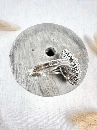 A navette shaped diamond cluster ring in white metal, sitting on top of a wooden and cloth object