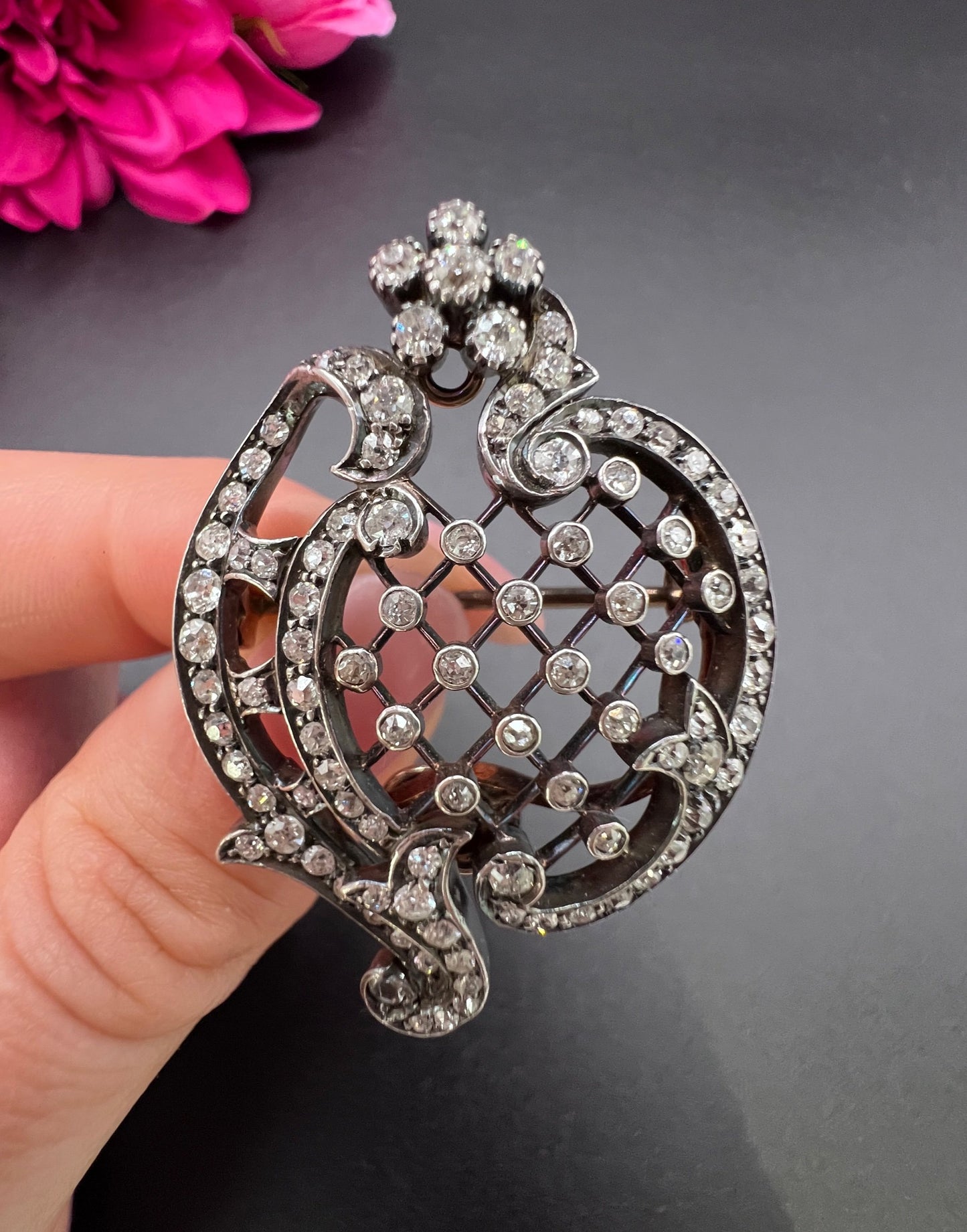 An openwork diamond set antique brooch in yellow gold and silver, held in a hand