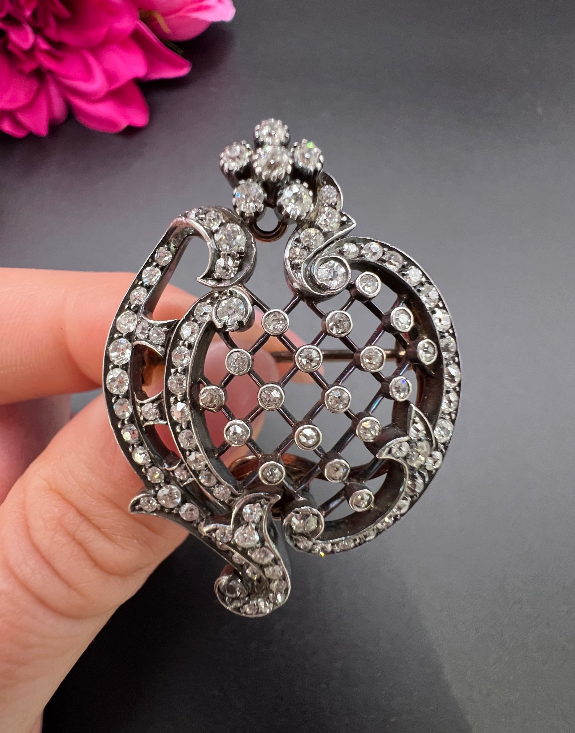 An openwork diamond set antique brooch in yellow gold and silver, held in a hand
