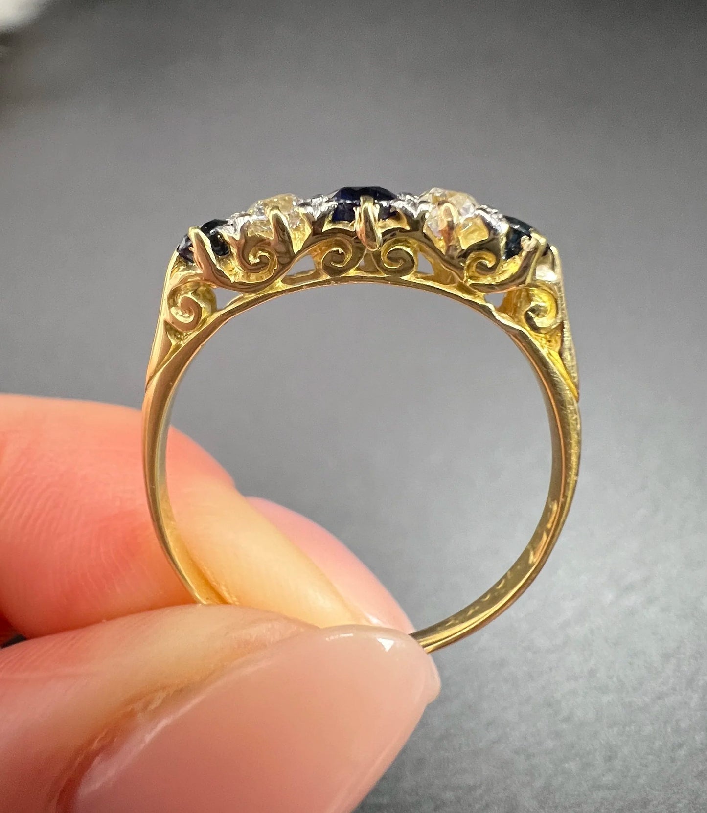 A yellow gold five stone sapphire and diamond carved half hoop ring, held in a hand