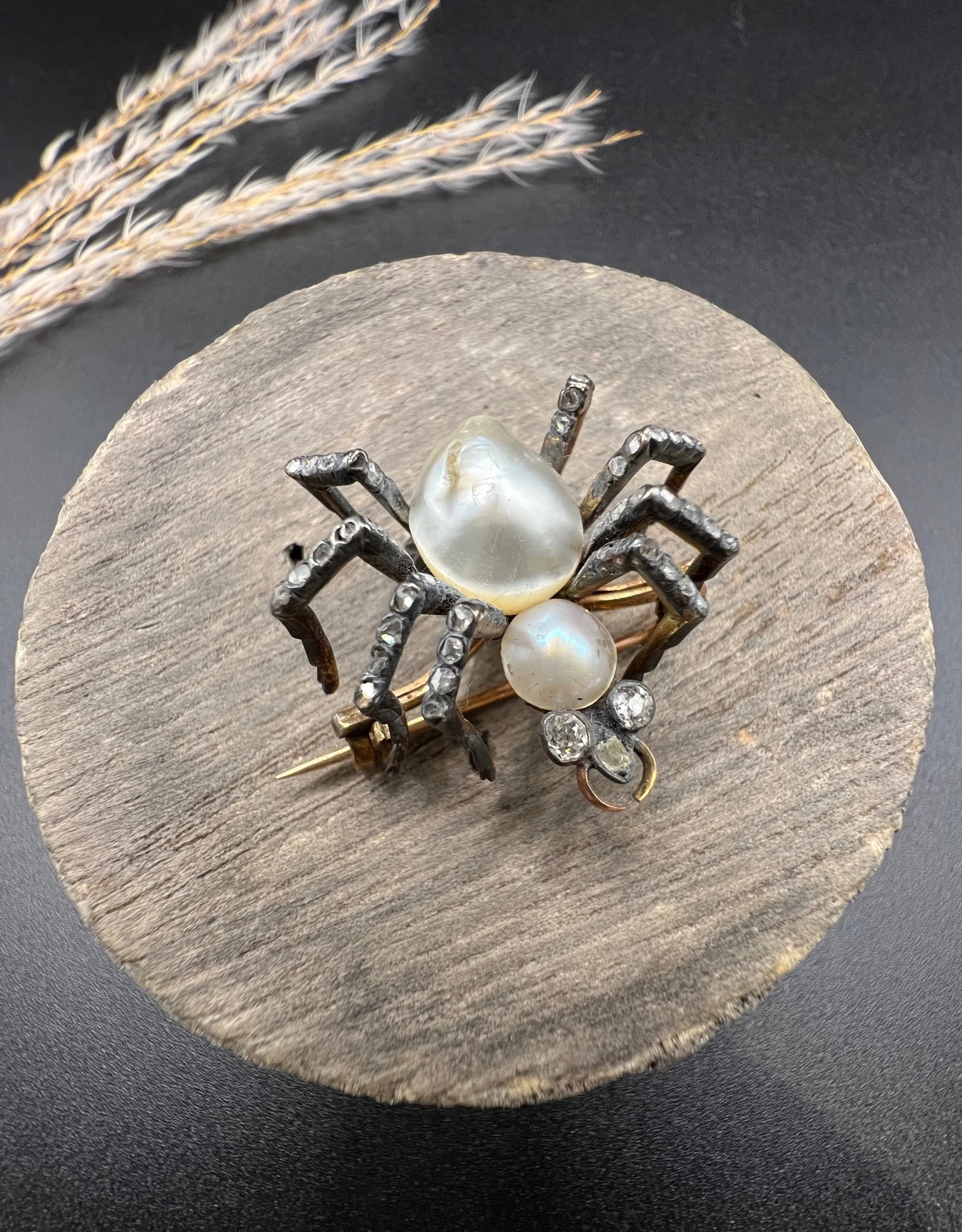 A pearl and diamond spider brooch in gold and silver, on a wooden spool