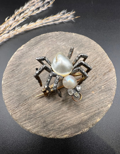 A pearl and diamond spider brooch in gold and silver, on a wooden spool