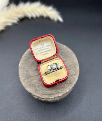A three stone diamond crossover ring, in a red antique ring box