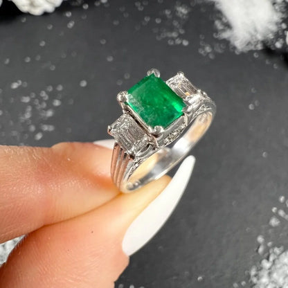 A three stone emerald and diamond ring in platinum, held in a hand