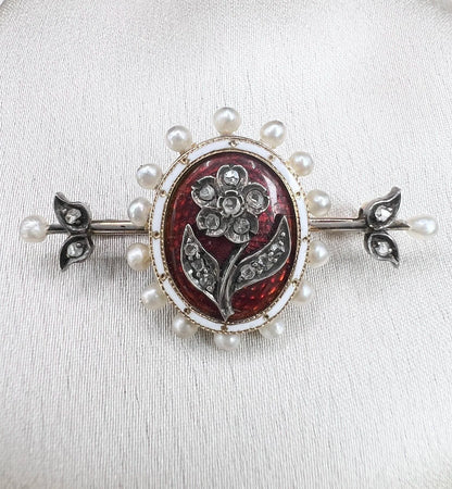 A yellow gold bar brooch with a red enamel centre surrounded by pearls, with a diamond flower motif and diamond leaves at either end