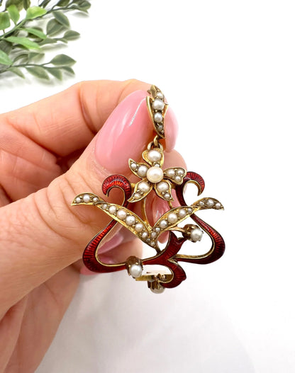 A floral pendant in yellow gold with seed pearls and red enamel, held in a hand