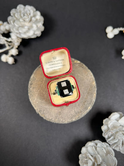 A geometric black onyx ring with diamonds and emeralds in white gold, in an antique ring box