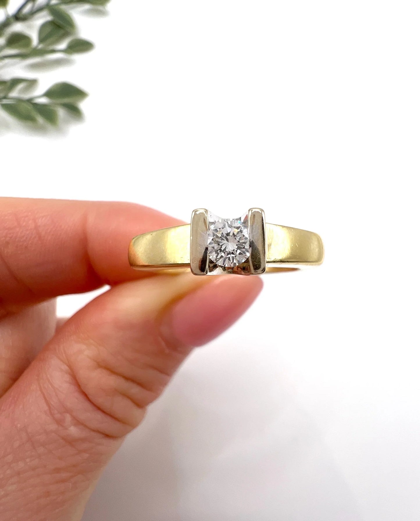 A brilliant cut diamond solitaire ring in yellow gold, held in a hand