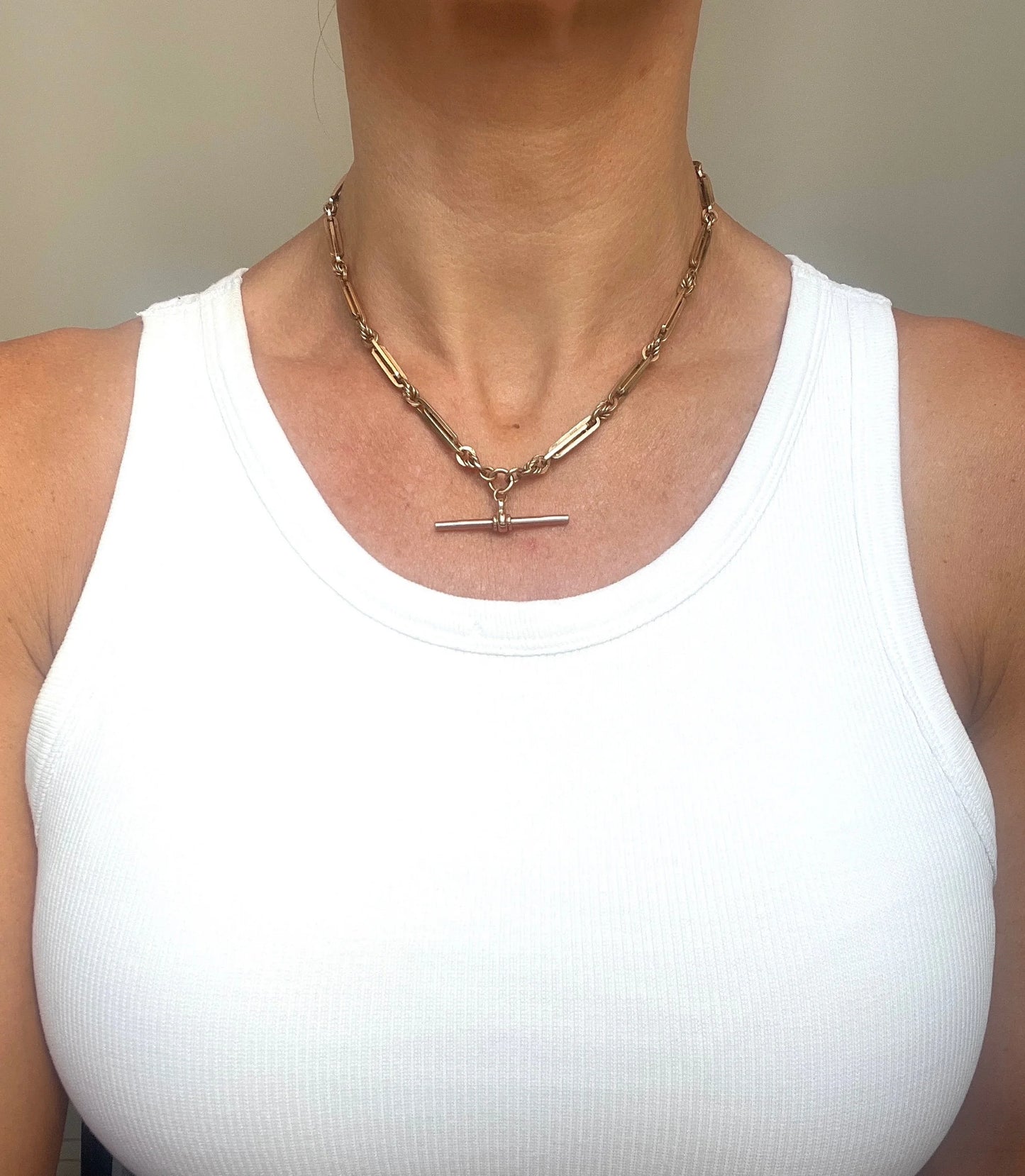 A rose gold fancy link Albert chain necklace, modelled by a woman wearing a white top