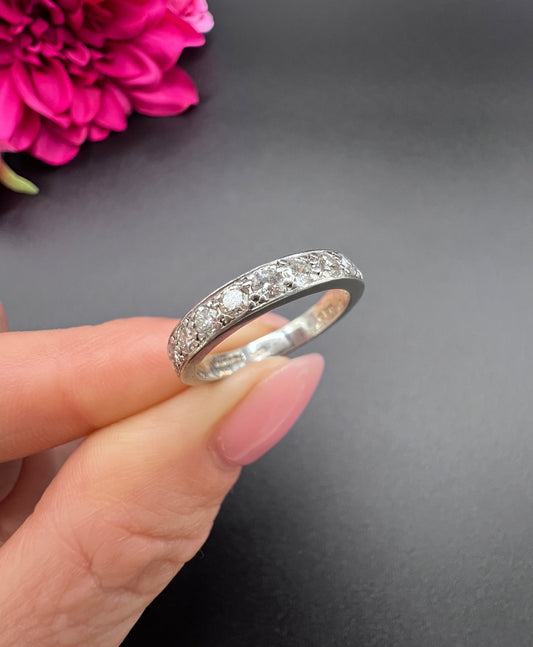 A platinum diamond set half eternity band ring, held in a hand