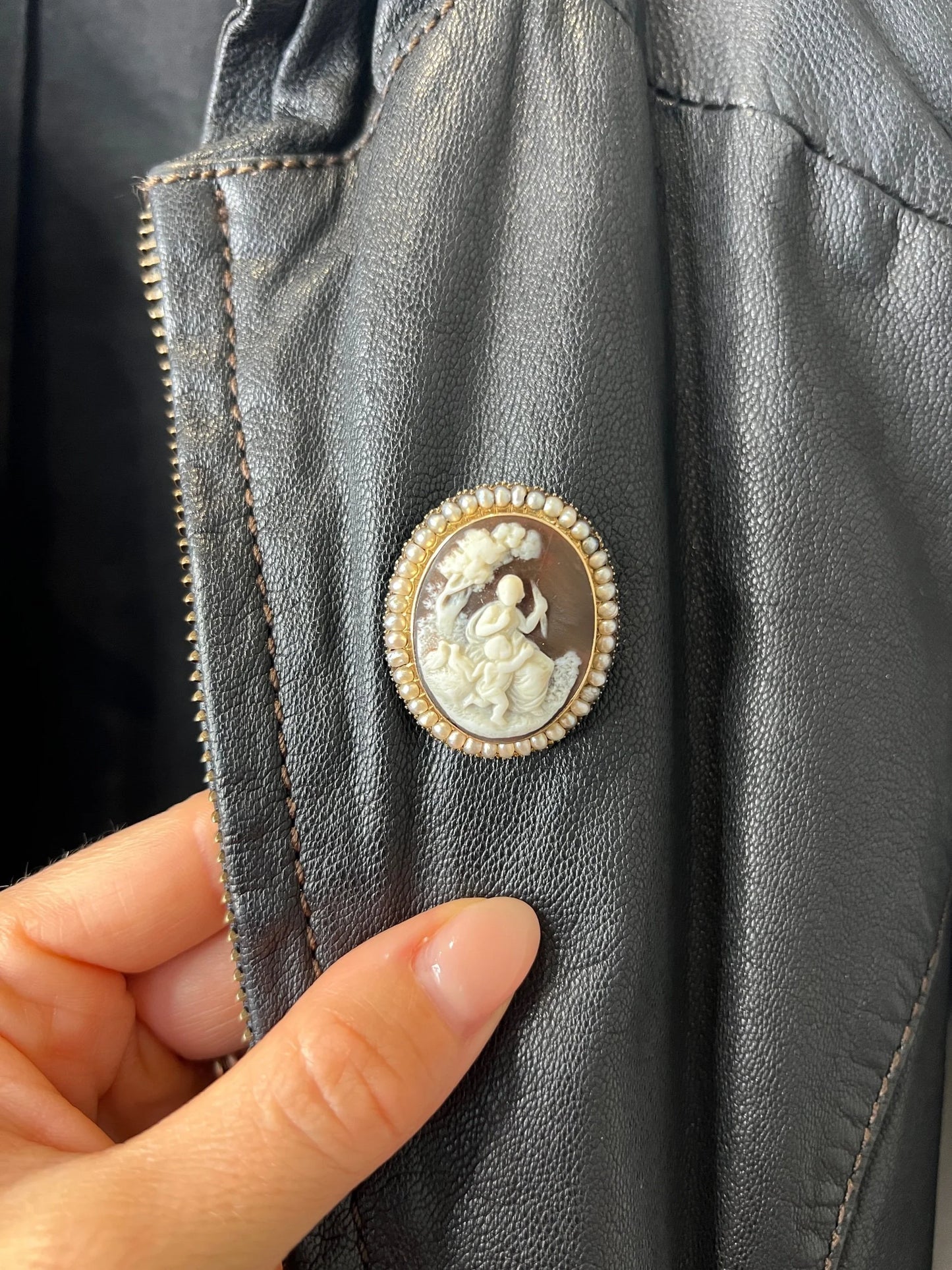 An antique oval cameo brooch depicting cherubs and birds, with a pearl border, set in gold, on a black jacket